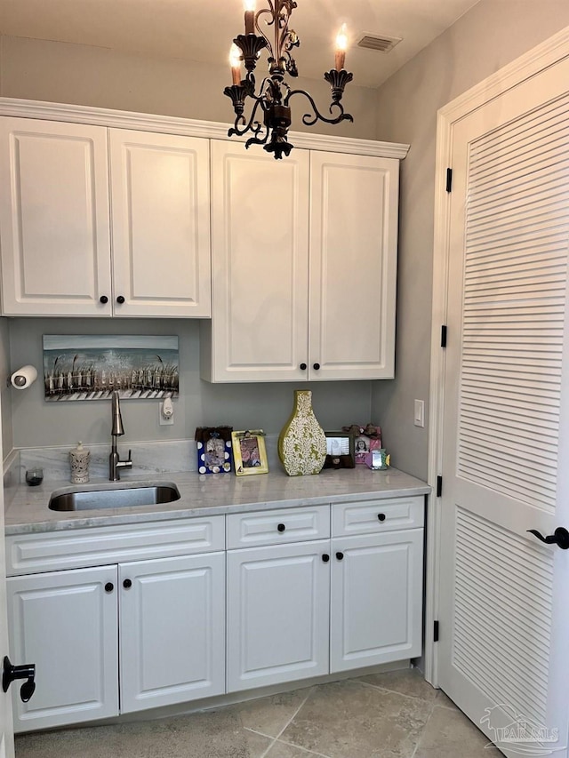 kitchen featuring sink, light stone counters, light tile patterned floors, and white cabinetry