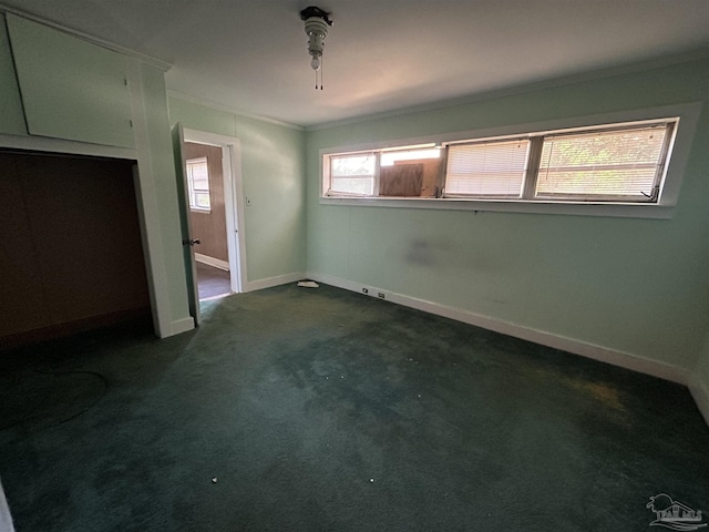 spare room with dark colored carpet, crown molding, and baseboards