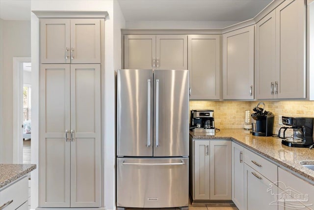 kitchen with light stone countertops, backsplash, gray cabinets, and stainless steel refrigerator