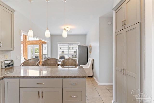 kitchen with decorative light fixtures, gray cabinets, kitchen peninsula, light tile patterned floors, and stone counters