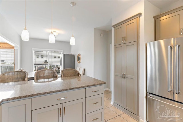 kitchen featuring hanging light fixtures, plenty of natural light, high end refrigerator, and light stone counters