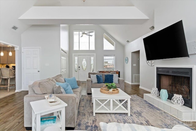 living room featuring wood-type flooring, a tiled fireplace, and high vaulted ceiling