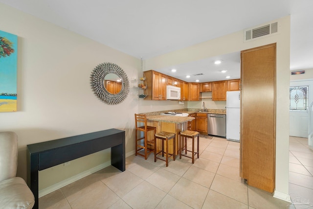 kitchen with white appliances, kitchen peninsula, a kitchen bar, light tile patterned flooring, and sink