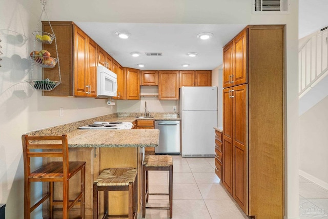 kitchen featuring white appliances, a kitchen breakfast bar, kitchen peninsula, light tile patterned floors, and sink