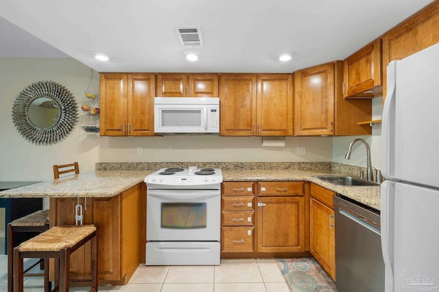 kitchen featuring sink, white appliances, light tile patterned floors, kitchen peninsula, and a breakfast bar area