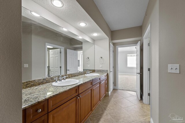 bathroom featuring a textured ceiling, tile patterned flooring, and dual bowl vanity