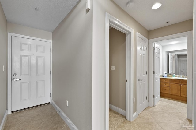 corridor featuring light tile patterned flooring, sink, and a textured ceiling