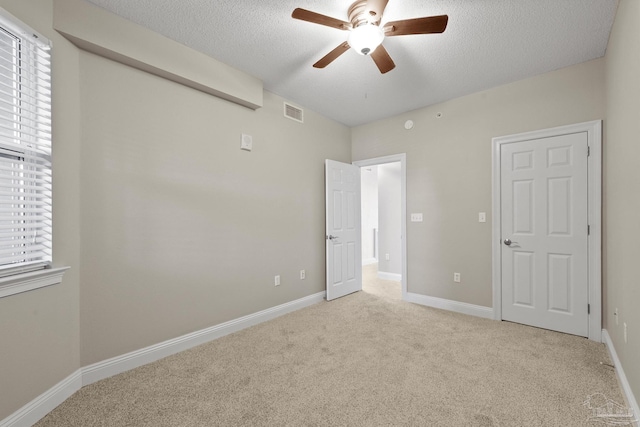 unfurnished bedroom with light colored carpet, a textured ceiling, and ceiling fan