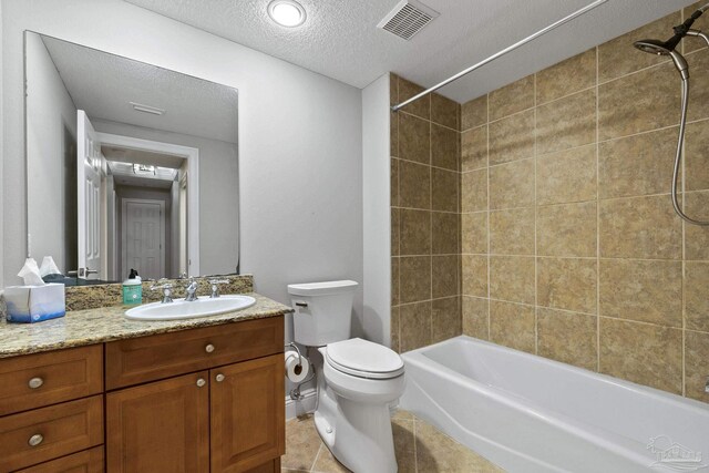 full bathroom with a textured ceiling, tiled shower / bath, toilet, vanity, and tile patterned floors