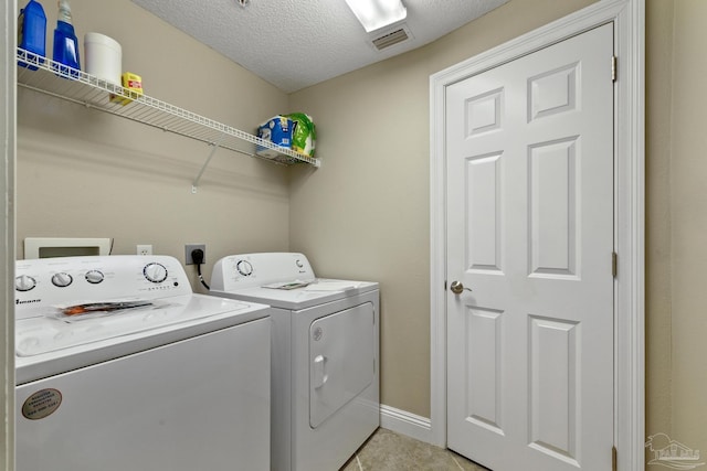 clothes washing area with washer and dryer, light tile patterned floors, and a textured ceiling