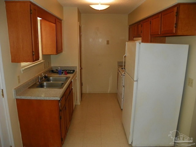 kitchen featuring brown cabinetry, washer / clothes dryer, freestanding refrigerator, light countertops, and a sink