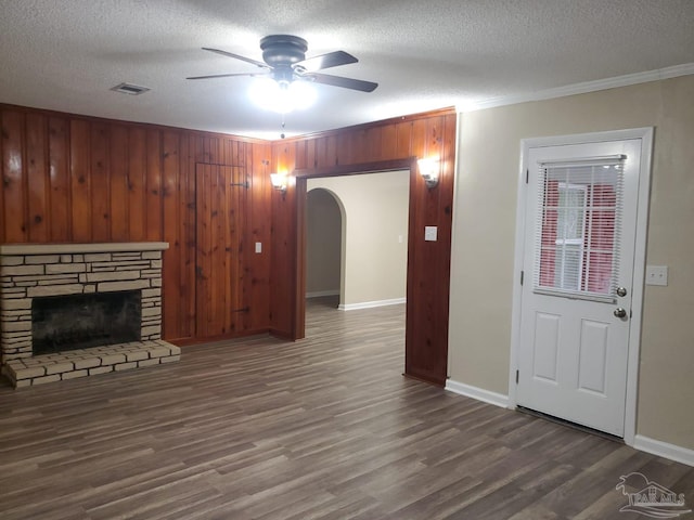 unfurnished living room with crown molding, ceiling fan, wood-type flooring, a textured ceiling, and a stone fireplace