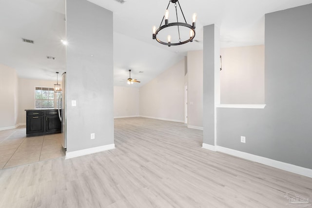 empty room with ceiling fan with notable chandelier, light hardwood / wood-style flooring, and vaulted ceiling