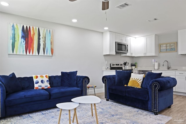 living room featuring ceiling fan, sink, and light hardwood / wood-style flooring