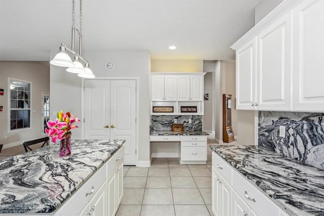 kitchen with built in desk, tasteful backsplash, white cabinets, dark stone counters, and decorative light fixtures