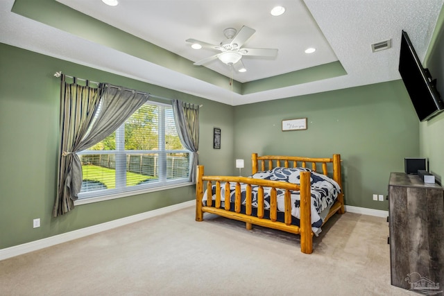 bedroom with ceiling fan, a tray ceiling, and light colored carpet