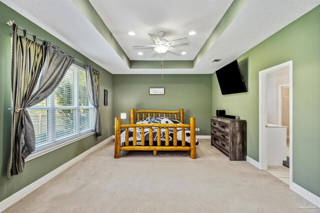 bedroom with light carpet, ceiling fan, and a tray ceiling