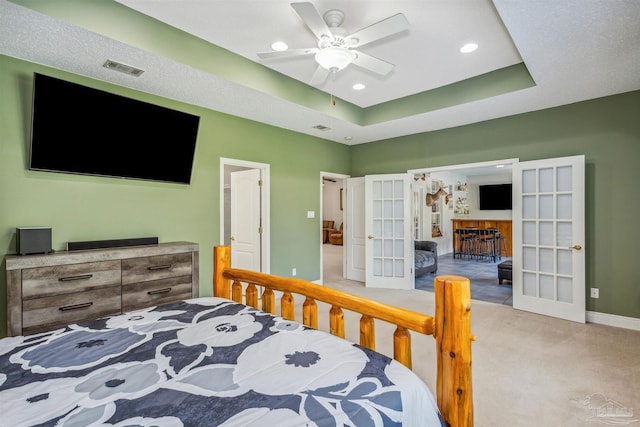 bedroom featuring ceiling fan, french doors, a raised ceiling, and light carpet