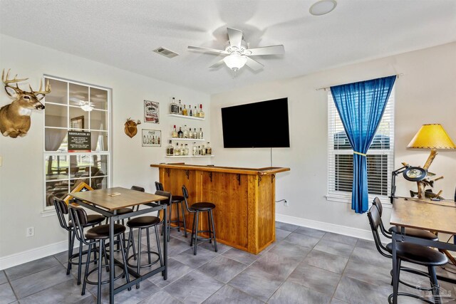 interior space featuring ceiling fan, a textured ceiling, and bar