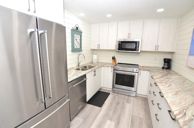 kitchen with stainless steel appliances, white cabinets, sink, light stone countertops, and light hardwood / wood-style floors