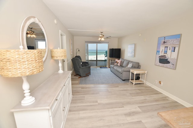 living area with a ceiling fan, light wood-style flooring, and baseboards