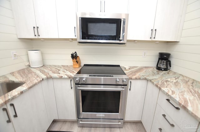 kitchen with appliances with stainless steel finishes, light stone countertops, white cabinets, and light hardwood / wood-style floors