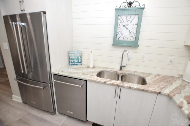 kitchen with wood walls, sink, appliances with stainless steel finishes, and light stone countertops