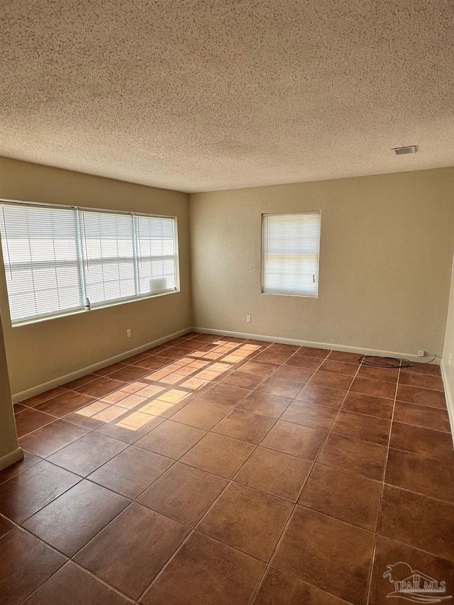 tiled empty room with a textured ceiling, visible vents, and baseboards