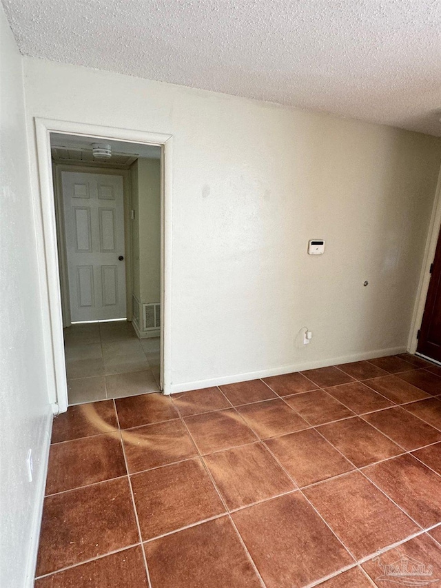 tiled empty room featuring baseboards and a textured ceiling