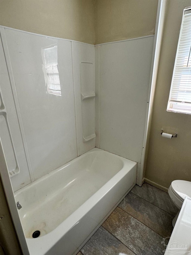 bathroom with toilet, a washtub, and baseboards