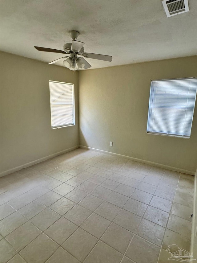spare room with tile patterned flooring, visible vents, ceiling fan, and baseboards