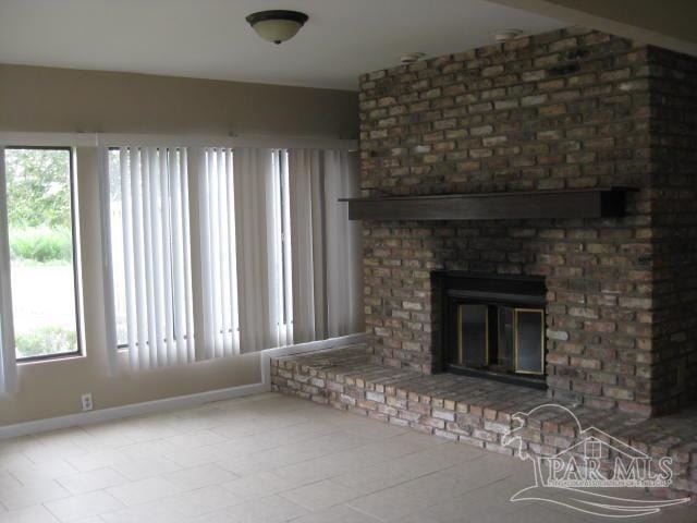 unfurnished living room featuring a brick fireplace and baseboards