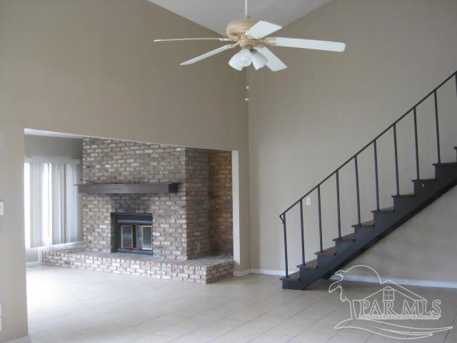 unfurnished living room featuring stairway, high vaulted ceiling, a brick fireplace, and ceiling fan