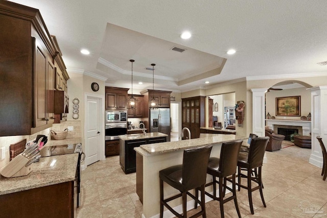 2926 Greystone Dr, Pace, FL 32571 - kitchen featuring ornate columns, a center island with sink, stainless steel appliances, a tray ceiling, and ornamental molding