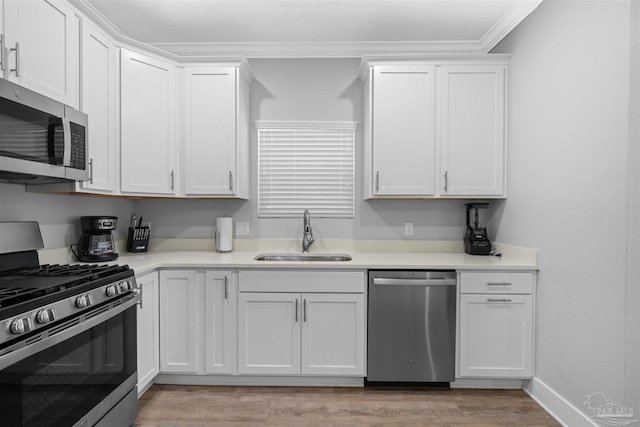 kitchen with appliances with stainless steel finishes, light wood-type flooring, sink, and white cabinets