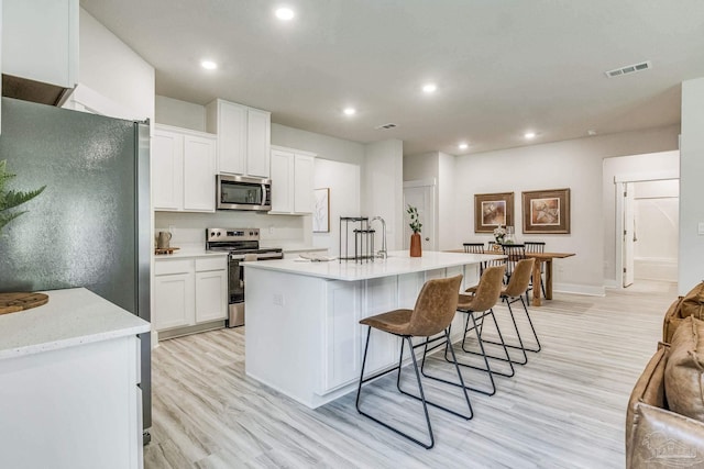 4680 Eider Rd, Pace, FL 32571 - kitchen featuring stainless steel appliances, recessed lighting, light wood-style flooring, white cabinetry, and a kitchen bar