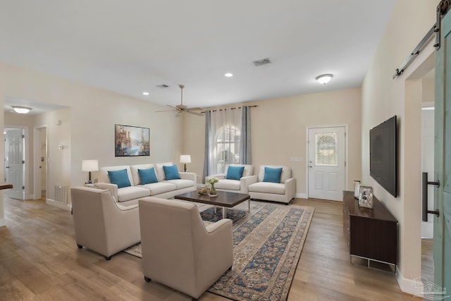 living room with ceiling fan, light hardwood / wood-style flooring, and a barn door