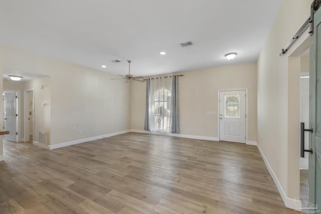 unfurnished room featuring ceiling fan, a barn door, and light hardwood / wood-style flooring