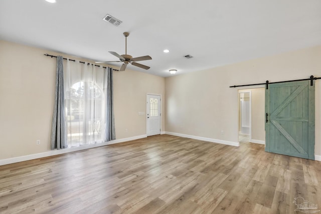 unfurnished room with ceiling fan, light hardwood / wood-style flooring, and a barn door