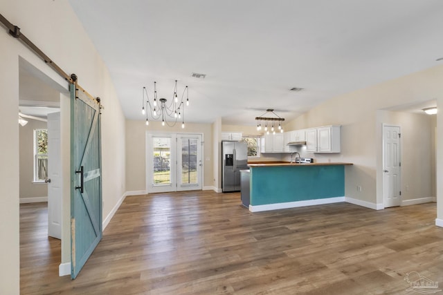 kitchen with stainless steel refrigerator with ice dispenser, white cabinetry, kitchen peninsula, vaulted ceiling, and a barn door