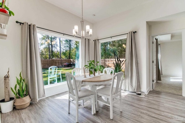 dining space with a notable chandelier, light wood-style flooring, baseboards, and lofted ceiling