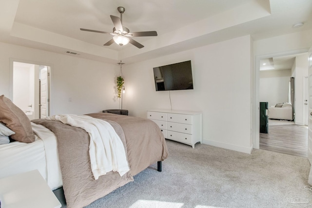 bedroom featuring light carpet, visible vents, a raised ceiling, and baseboards