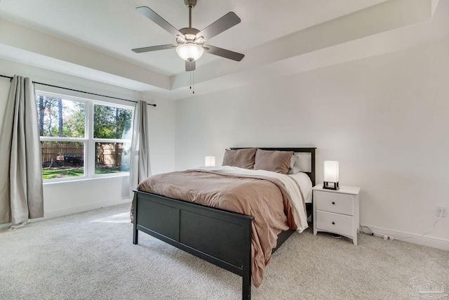 bedroom with light colored carpet, baseboards, a tray ceiling, and ceiling fan