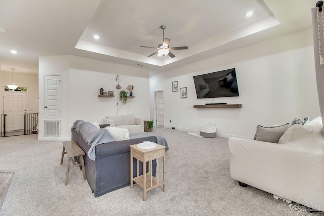 living area with a tray ceiling, light colored carpet, and visible vents