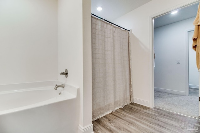 bathroom with baseboards, a shower with curtain, wood finished floors, and a bathtub