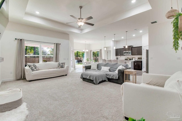 living area featuring baseboards, a tray ceiling, light carpet, recessed lighting, and ceiling fan with notable chandelier