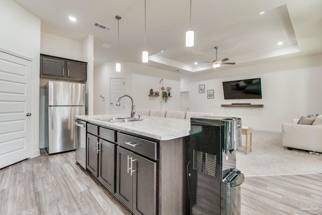 kitchen featuring open floor plan, light countertops, a tray ceiling, stainless steel appliances, and a sink