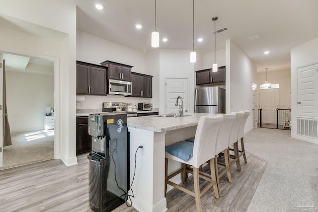 kitchen featuring visible vents, dark brown cabinetry, appliances with stainless steel finishes, a kitchen breakfast bar, and a sink