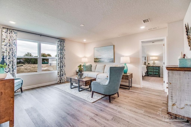 living room featuring visible vents, a textured ceiling, baseboards, and wood finished floors