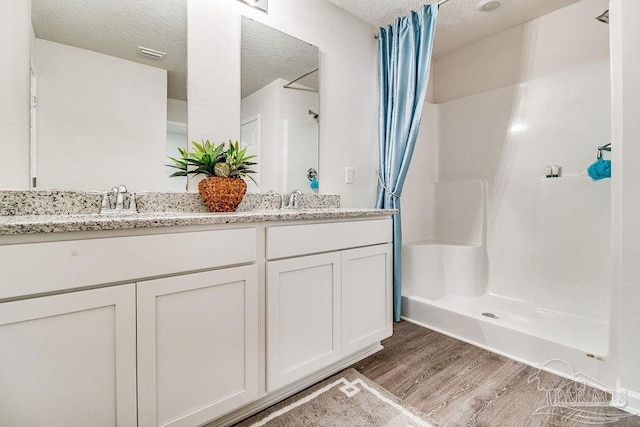 bathroom with double vanity, a sink, a textured ceiling, wood finished floors, and a shower with curtain